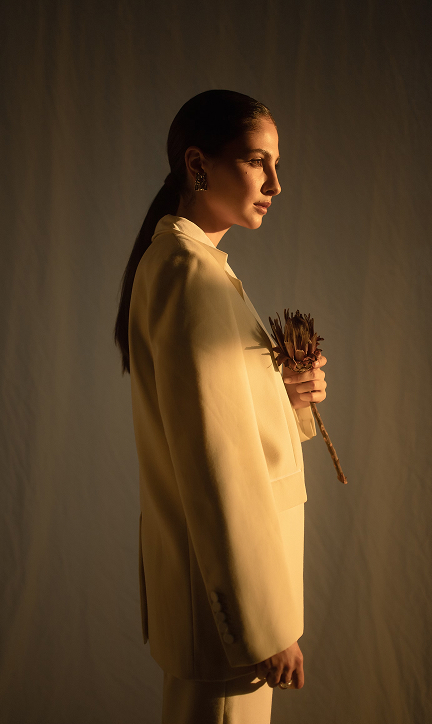 A sophisticated woman in a white jacket, standing with a flower in hand.
