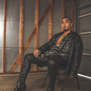 A stylish man wearing a leather outfit, sitting confidently in a garage.