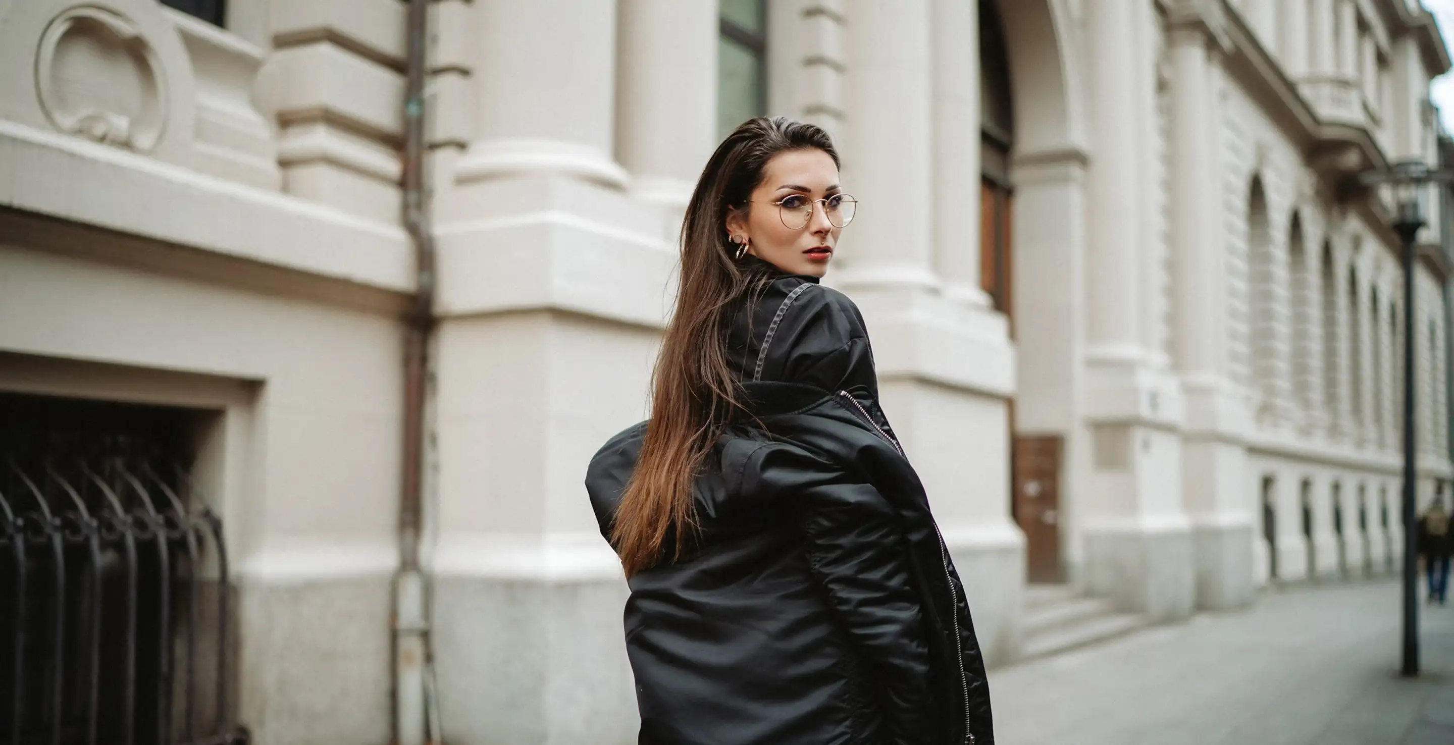 A fashionable woman on a city street wearing a black coat and stylish accessories.