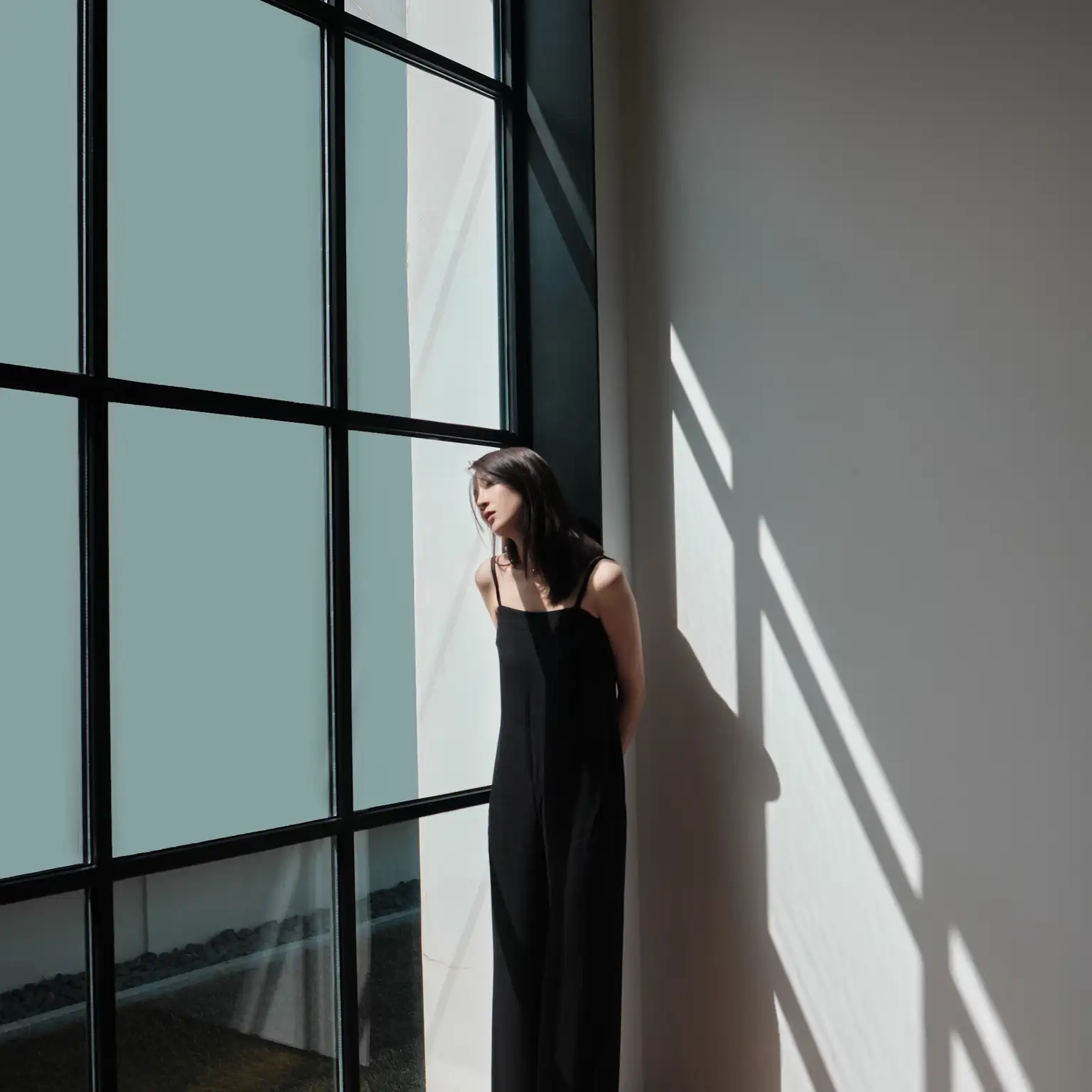 A stylish woman standing by a modern window in a minimalist interior space.