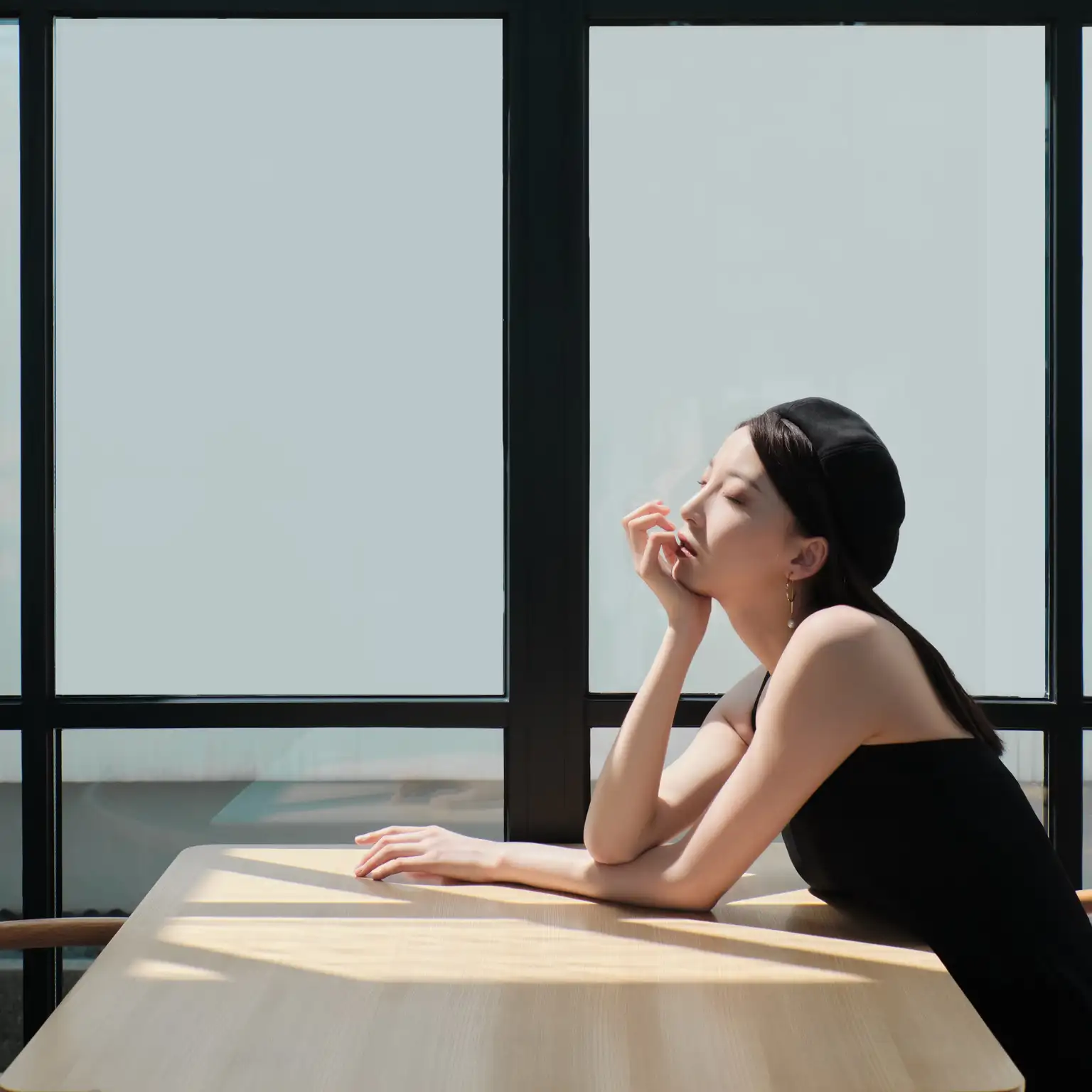 A thoughtful woman resting her chin on her hand while sitting at a table by a window.