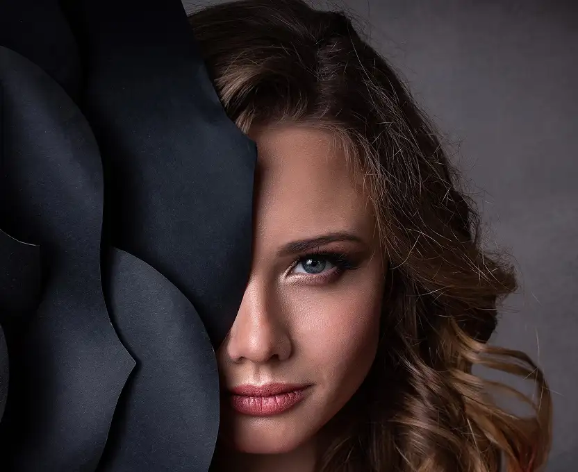 Expressive portrait of a woman with striking features, partially concealed by black paper, emphasizing her eyes.