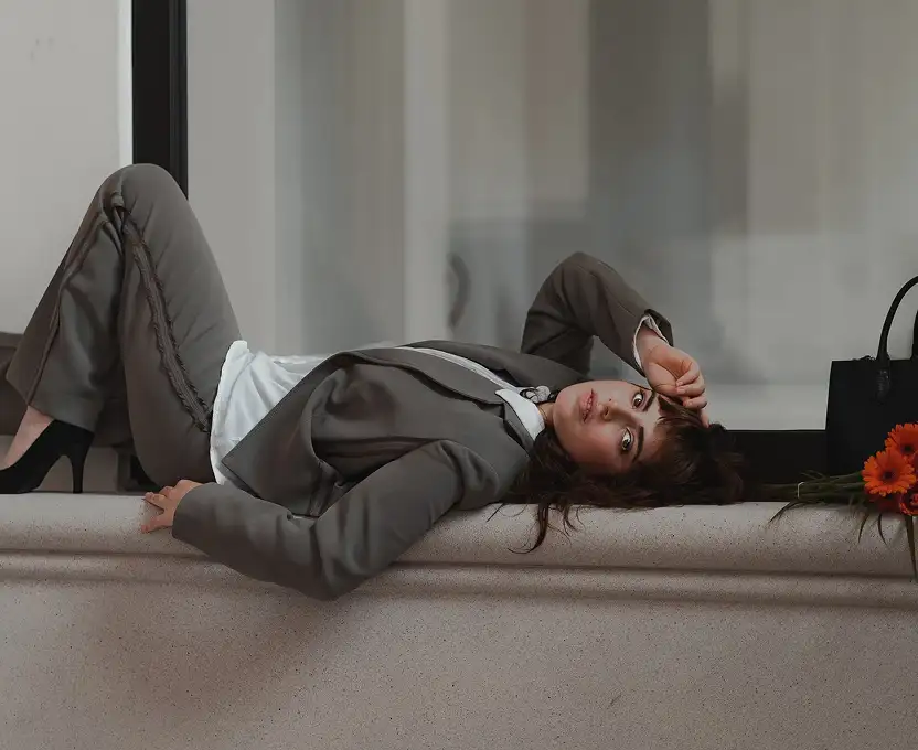 A woman in a stylish gray business suit lounging on a ledge with a flower beside her.
